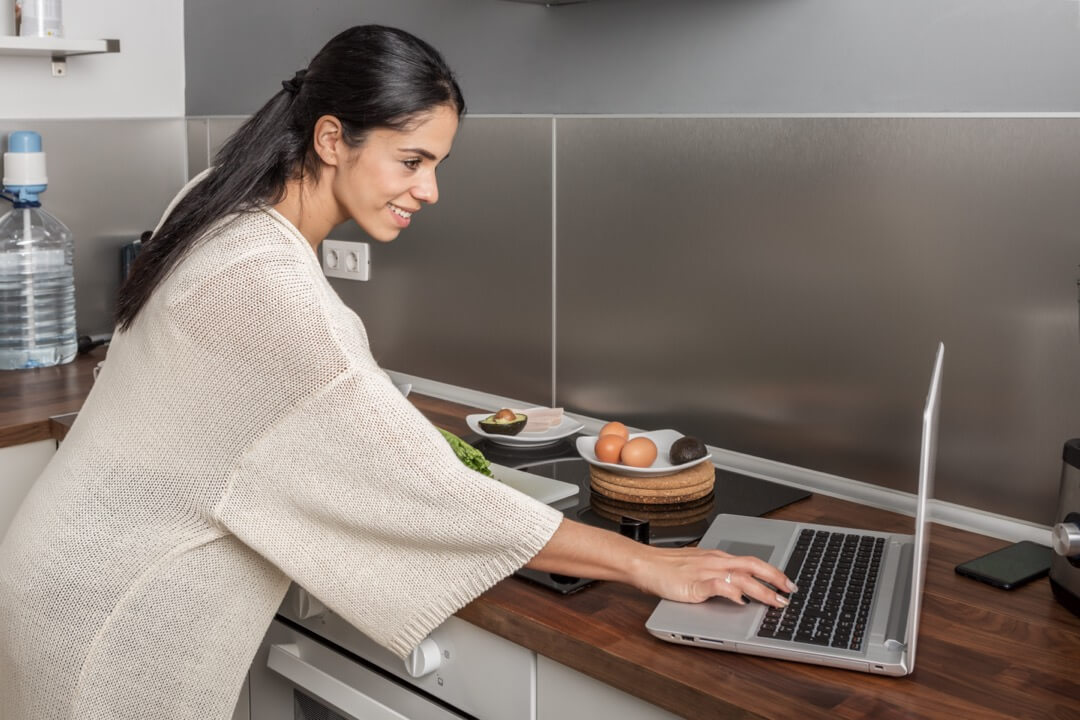 Femme souriante sur son laptop dans une cuisine moderne.